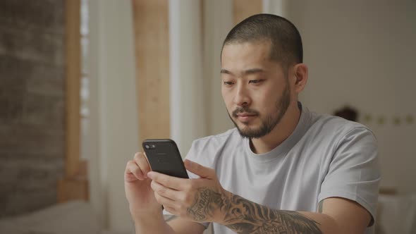 20s Tottoed Asian Man Swiping on His Smartphone with Various Facial Expressions