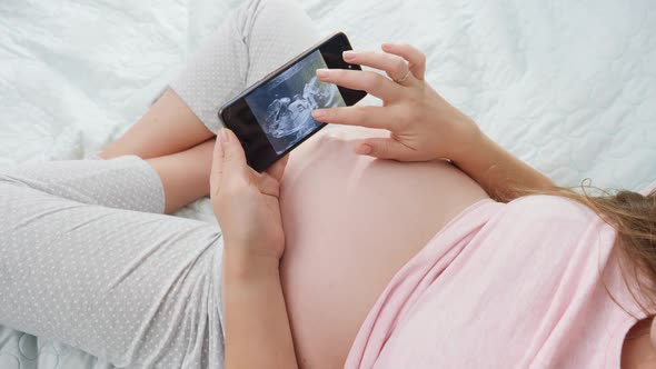 Closeup of Pregnant Woman Looking on Ultrasound Image of Her Unborn Child and Stroking Big Belly