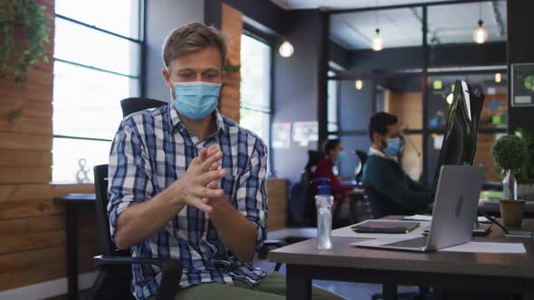 Caucasian man wearing face mask using hand sanitizing at modern office