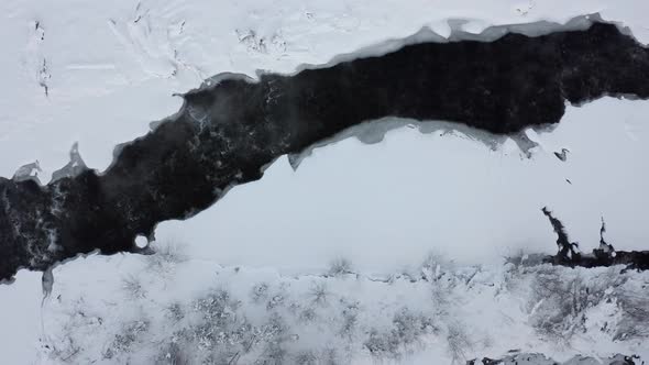 Bialka river flowing between snowy and frozen banks, Poland. Aerial top-down sideways