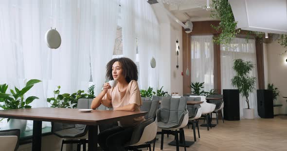 Long Shot American Young Beautiful Girl with Curly Afro Hair Black Woman Sits at Table in Expensive