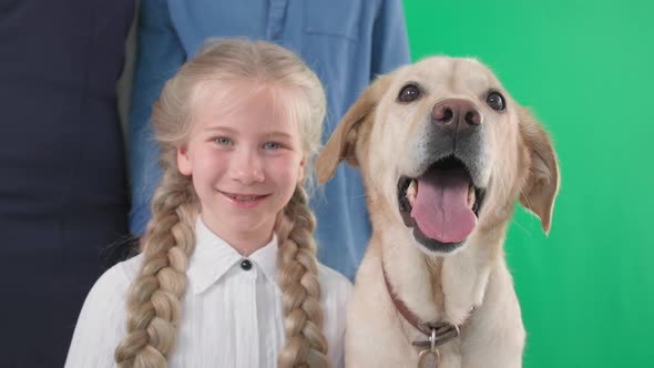 Happy Childhood Cute Little Girl with Dog and Parents Smiling and Looking at Camera on Green