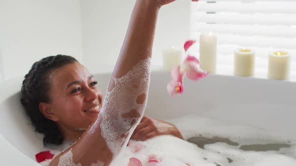 African american woman playing with rose petals in the bath tub in the bathroom at home