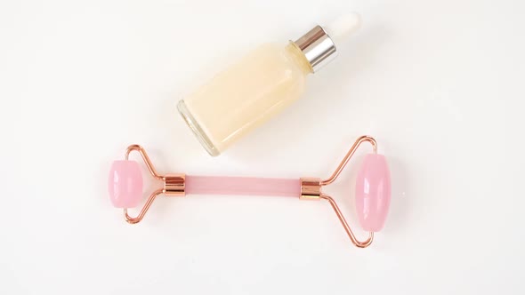 Rotation of Pink Quartz Facial Roller and Glass Bottle with Gel Fluid Isolated on White Background