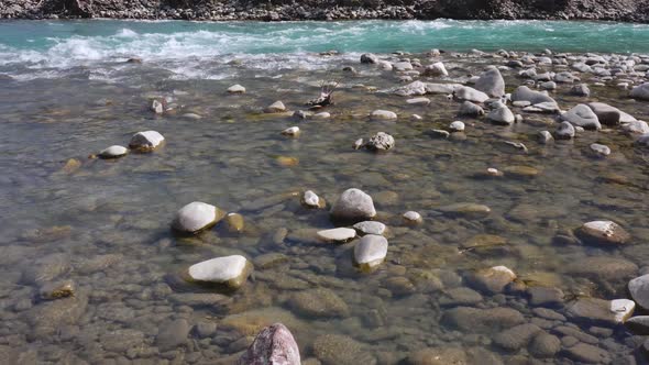 Drone flying low over crystal clear blue waters of fresh flowing rocky stream.