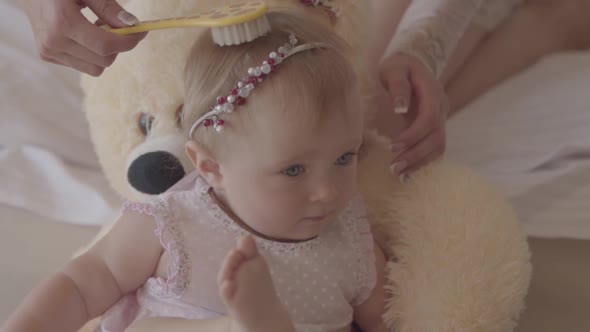 Little Baby Girl in a Pink Dress Lying on the Bear Toy at Home While the Hands of Her Mother