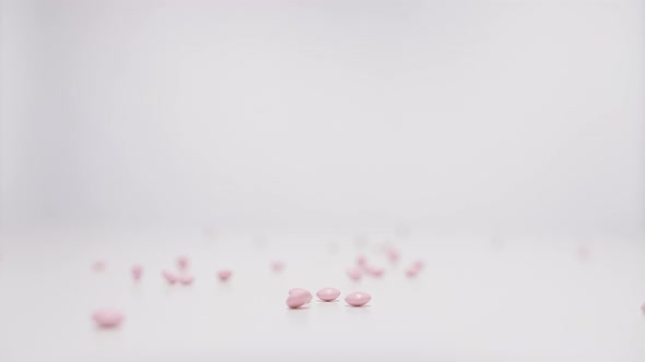 Rose pills falling on white background in slow motion.