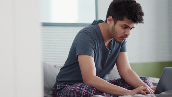 Serious Indian man wearing pajama typing by laptop