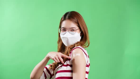 Young Asian woman pointing to her arm after being vaccinated against covid-19 in studio with chroma