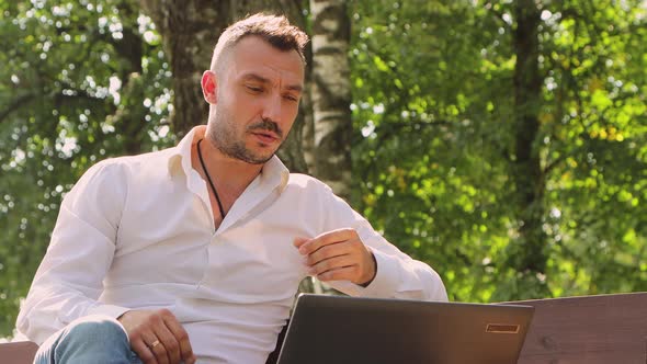 Business Man in a White Shirt Talking Online in a Laptop on a Bench
