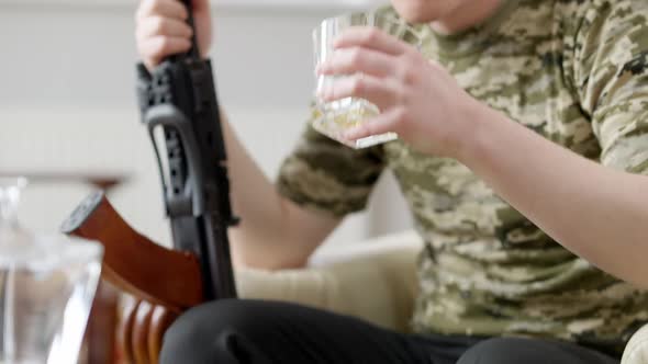 Camera Follows Glass with Scotch Male Young Soldier Drinking Whiskey Holding Gun