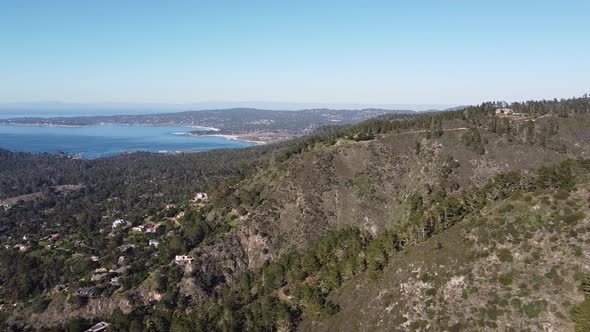 Small town on forestry hillside with beautiful blue bay in horizon, high angle drone view