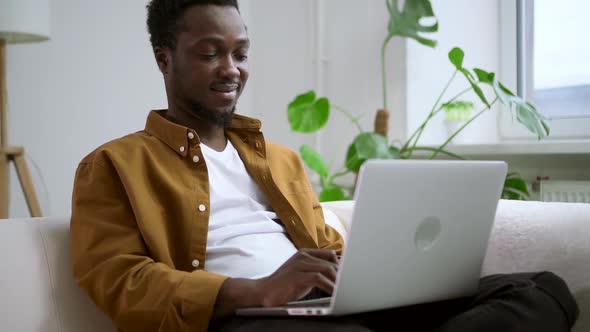 Smile African Man Typing Text on Laptop Keyboard on Couch at Home Spbas