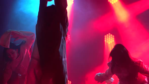 Three Charming Girls in White Shirt Are Dancing on the Stage. Silhouettes in a Dark Studio with