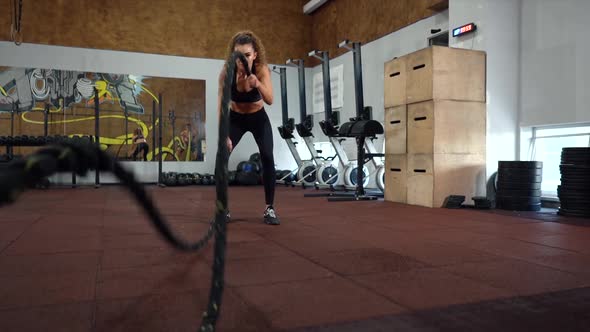 Athletic young woman doing crossfit exercises with a rope in gym. Slow motion