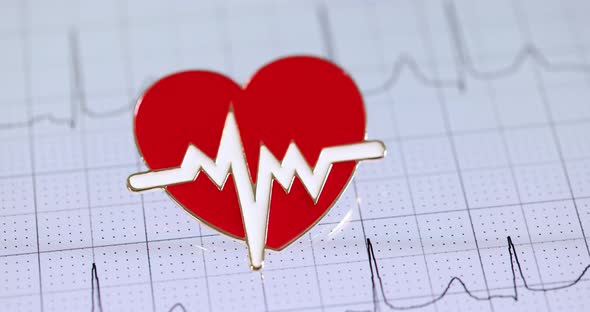 Red Heart Shaped Icon Lying on Paper with Electrocardiogram Closeup  Movie Slow Motion