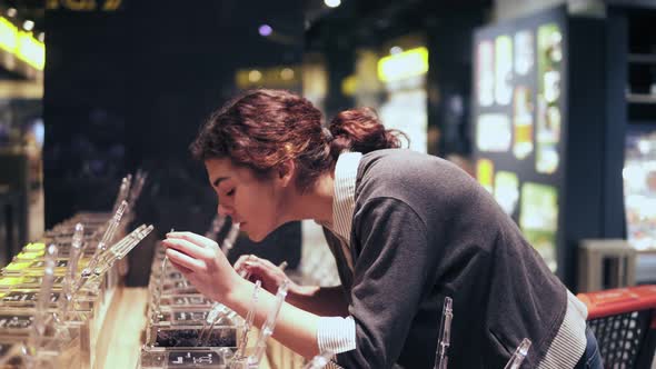 Young Beautiful Brunette Girl Smells Tea Before Buying It in Grocery Store