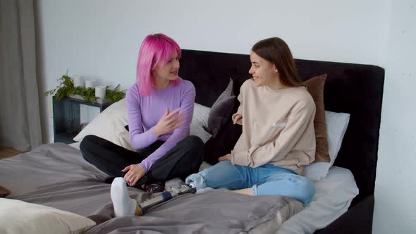 Joyful Pink Haired Female and Friend with Congenital Disability Talking on Bed