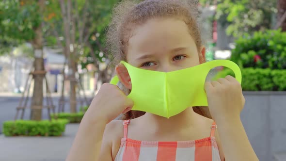 Pandemic Portrait of a Little Girl with a Sad Face in a Protective Mask on the Street in the City