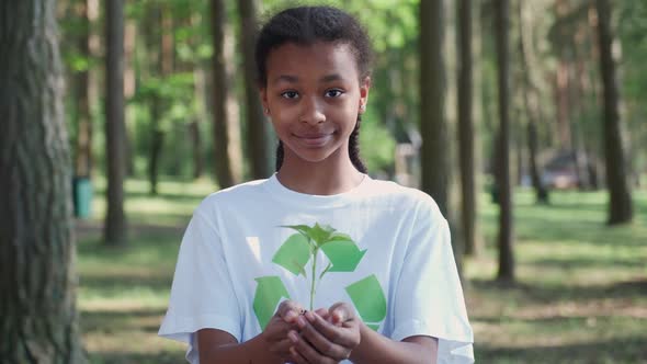 Young African Female Volunteer Holds a Small Flower Plant in Her Hands and Looks at the Camera a