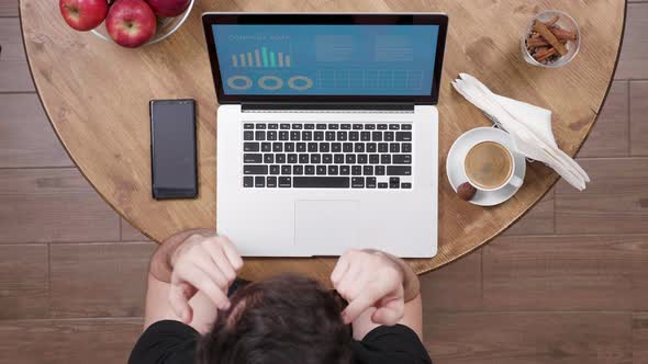 Young Entrepreneur in a Coffee Shop Looking at Charts and Graphs at His Laptop