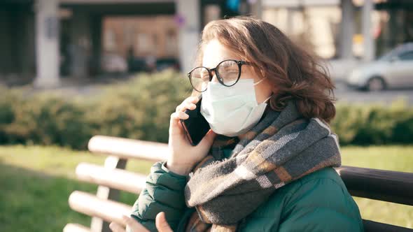 Close-up Shot of a Young Woman in Glasses and Medical Mask Talking on Her Phone