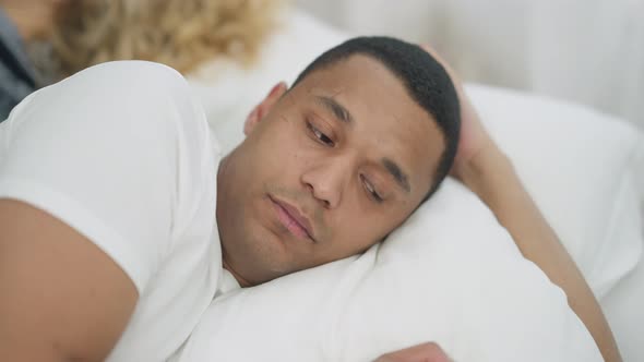 Closeup Portrait of Sad Young Handsome African American Man Lying in White Bed Looking Over Shoulder