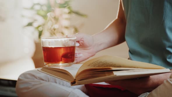 Woman Holding Steaming Cup of Tea or Coffee and Reading a Book.