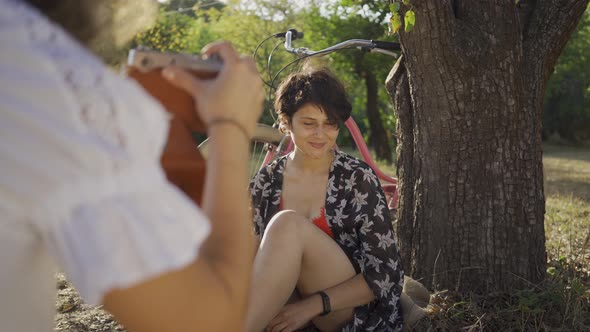 Attractive Young Woman with Short Hair Sitting Under the Tree While Her Friend Taking Photo