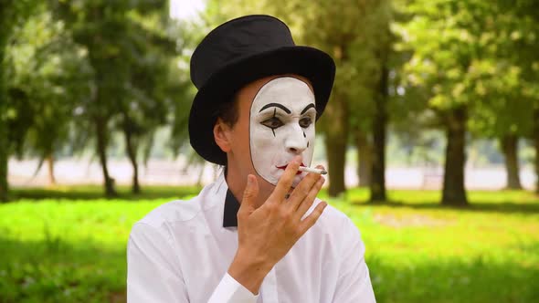Mime in a Black Hat Smokes Outdoors. Bad Habits