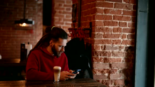 Informal Young Man is Resting Alone in Cafe and Listening to Music By Smartphone