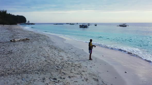 Male model fishing alone on tranquil coast beach lifestyle by aqua blue sea with white sandy backgro