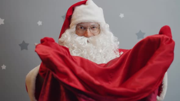 Slow Motion of Smiling Guy in Santa Claus Costume Giving Bag with Gifts To Camera