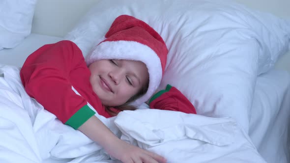 Happy Little Girl in Santa Hat and Red Pajama Wakes Up on Christmas Morning Waiting for a Present