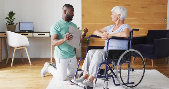 Video of happy african american male physiotherapist examining caucasian senior woman on wheelchair