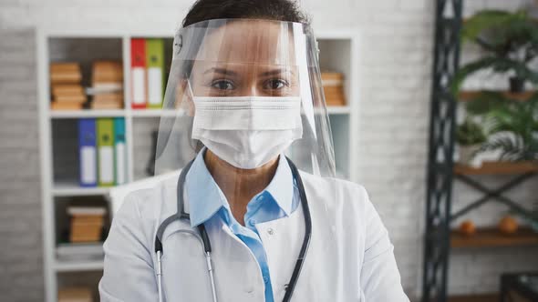 Doctor Female in Protective Mask and Face Shield is Smiling and Looking at you While Standing at