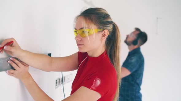 Girl in Goggles Checks Wall Level and Man Listening To Music