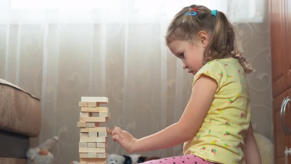 Curly-haired, blonde four-year-old girl is playing jenga game