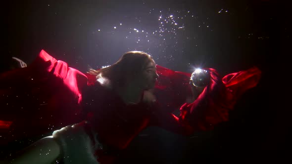A Woman in a Red Christmas Costume Is Deep Under the Water on a Dark Background Floating Creating a