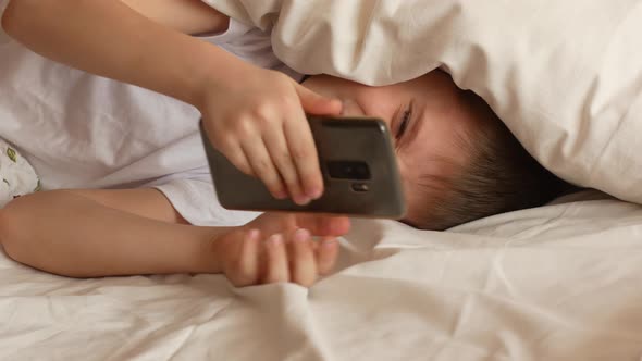Caucasian boy, 7-9 years old, in bed, covering his ears with a pillow, does not want to wake up afte