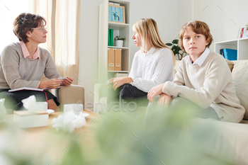 g to psychologist about teenage son while angry boy deep in thoughts looking away, mother and adolescent son having problem with mutual understanding