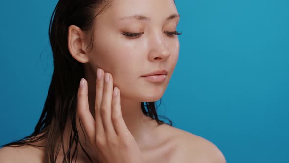 Young Pretty Woman with No Make-up and Clean Skin Applying Cream on Cheek and Looking To the Side