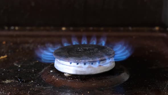 Dirty old gas stove. The burner on the stove burns with a blue flame