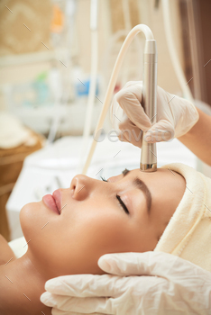 ment table with closed eyes while highly professional cosmetologist making cavitation rejuvenation skin treatment