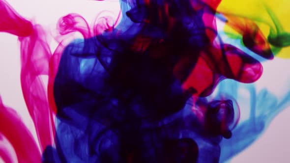 Different colors of ink squirted into water as it mixes and spins alt