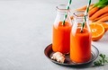 Fresh carrot, ginger and orange drink in glass bottles on a gray stone background - PhotoDune Item for Sale