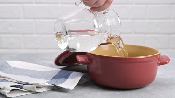 Pouring clean water from a glass jug into a pot.