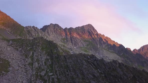 Ascending aerial view reveals amazing rugged landscape with red, orange and purple light of sunset o