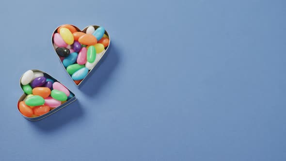 Video of overhead view of multi coloured sweets in two heart shapes with copy space over blue
