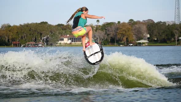 A young woman wake surfing behind a boat on a lake.